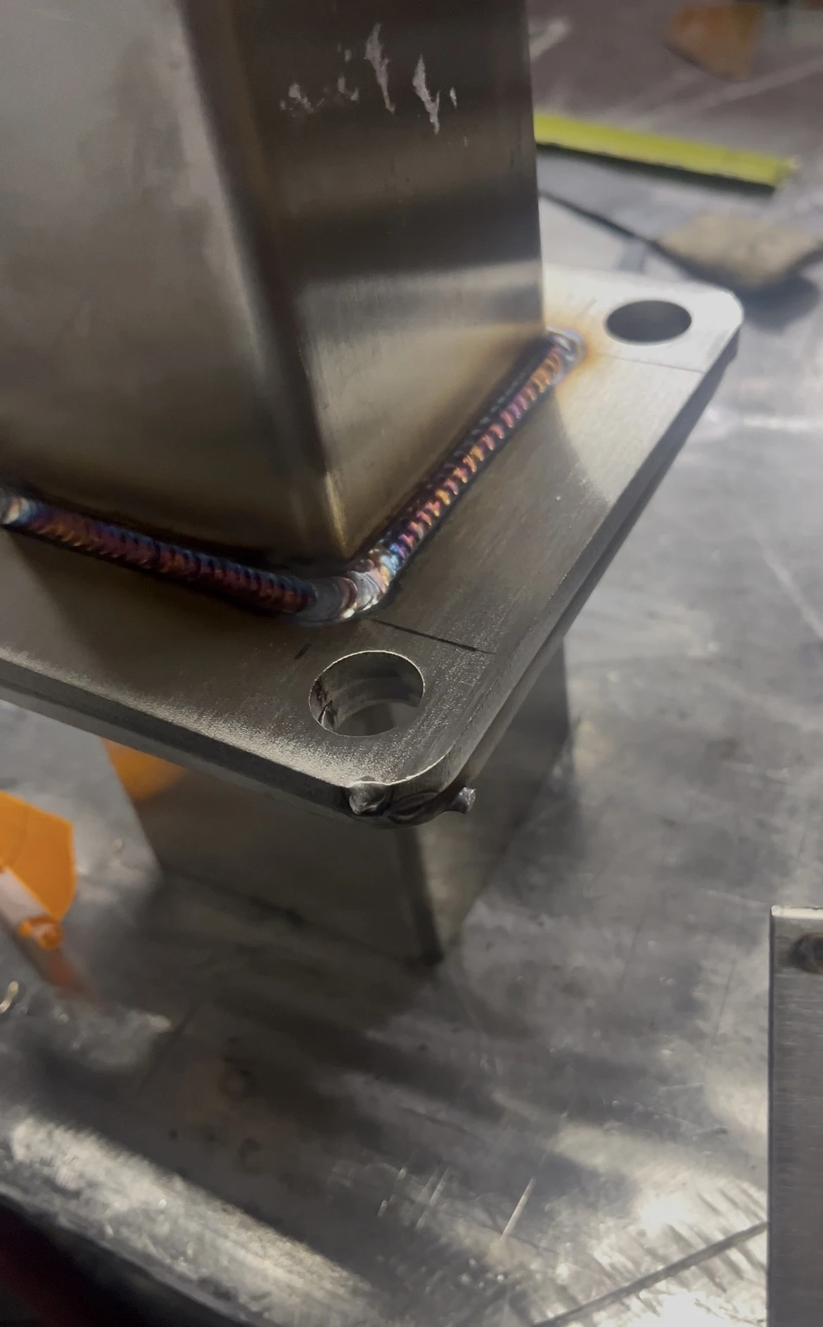 Weld wrapping around a rectangular metal corner on a drilled base plate