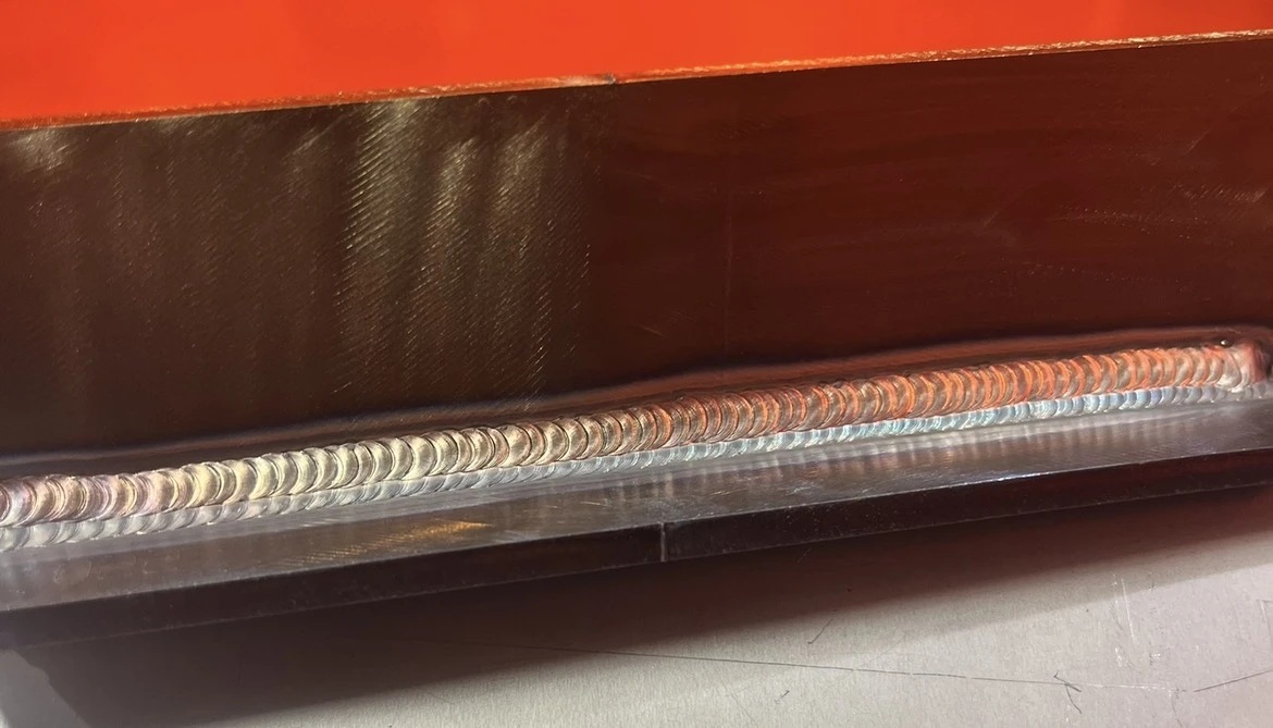 A long welded plate joint photographed closely across a workshop bench